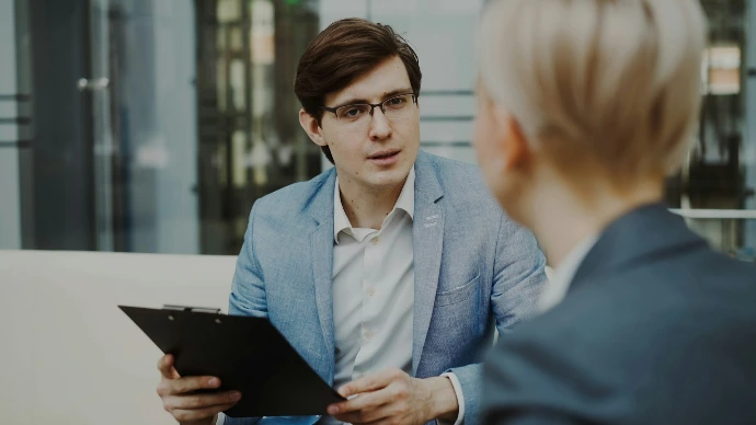 Man in suit holding clipboard talking to woman